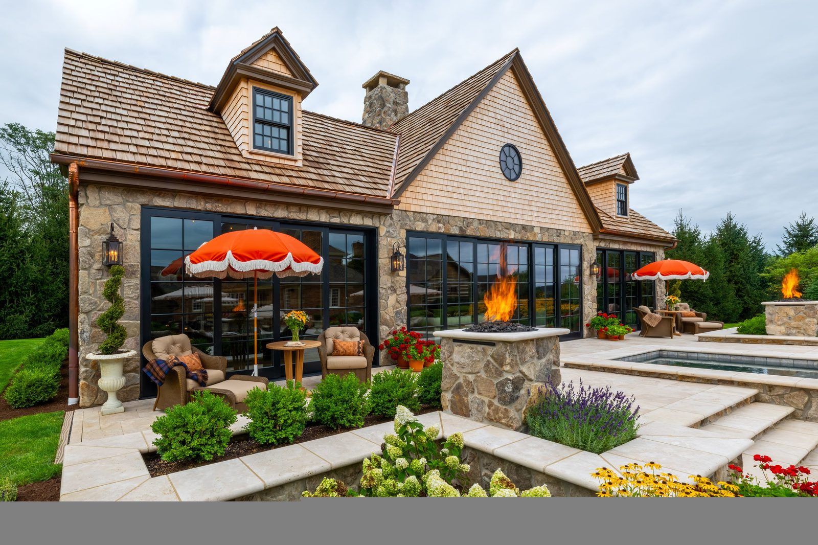 Pool house front in daylight with cedar shake roof, stone walls, and orange umbrellas