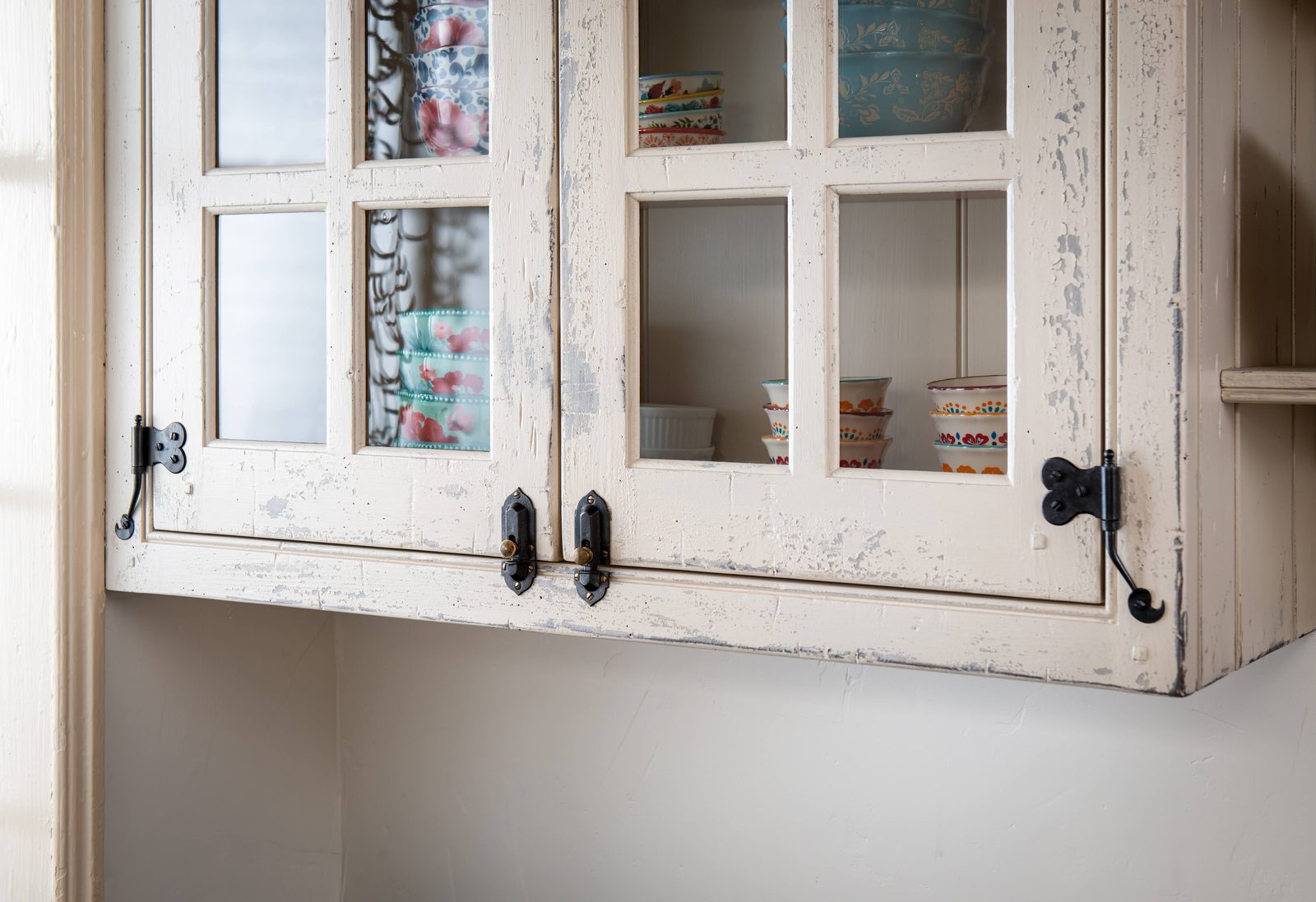 Weathered white glass-front cabinetry with antique iron hardware