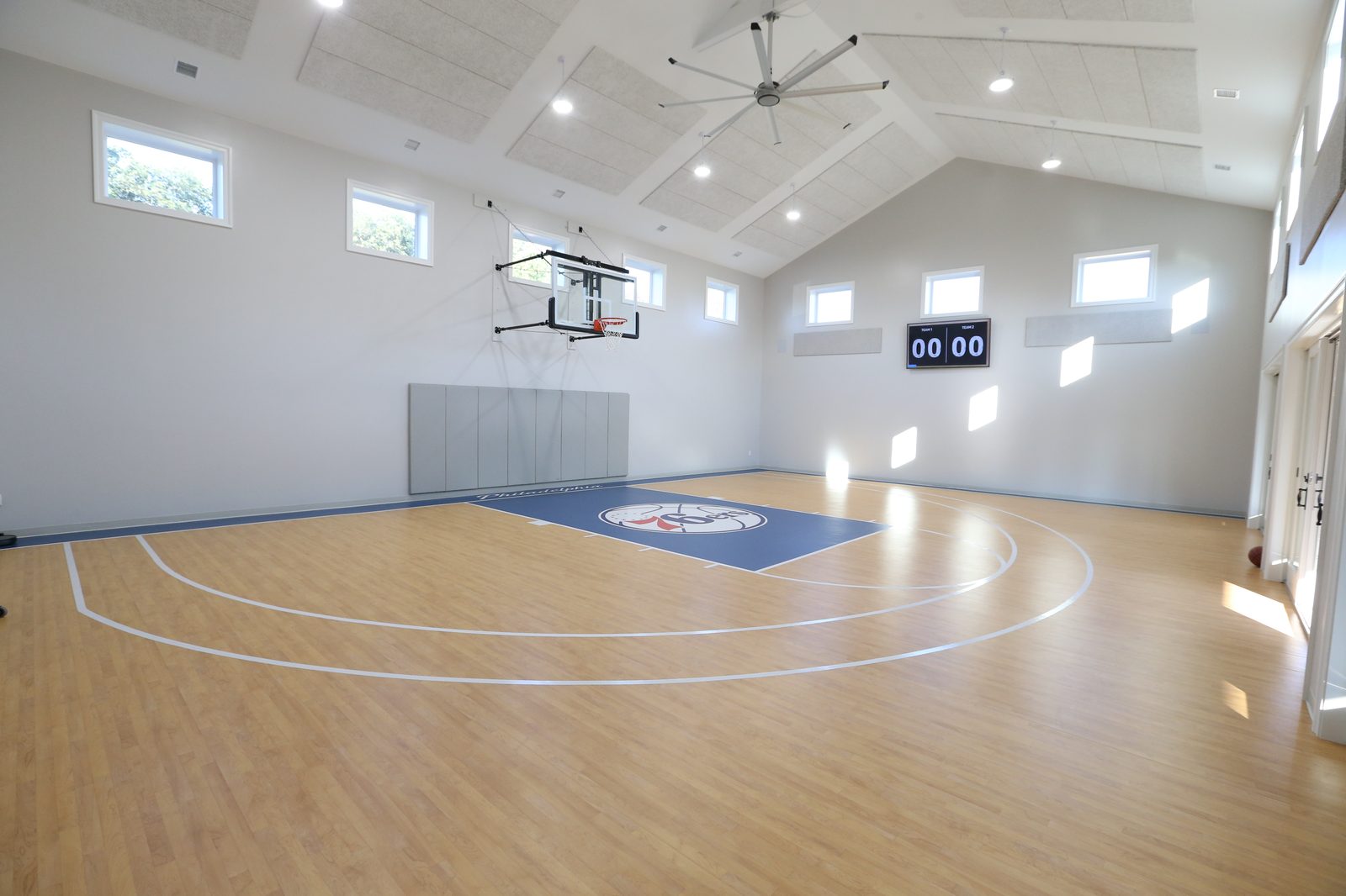 Indoor basketball court with vaulted ceiling, scoreboard, and Sixers-inspired graphics