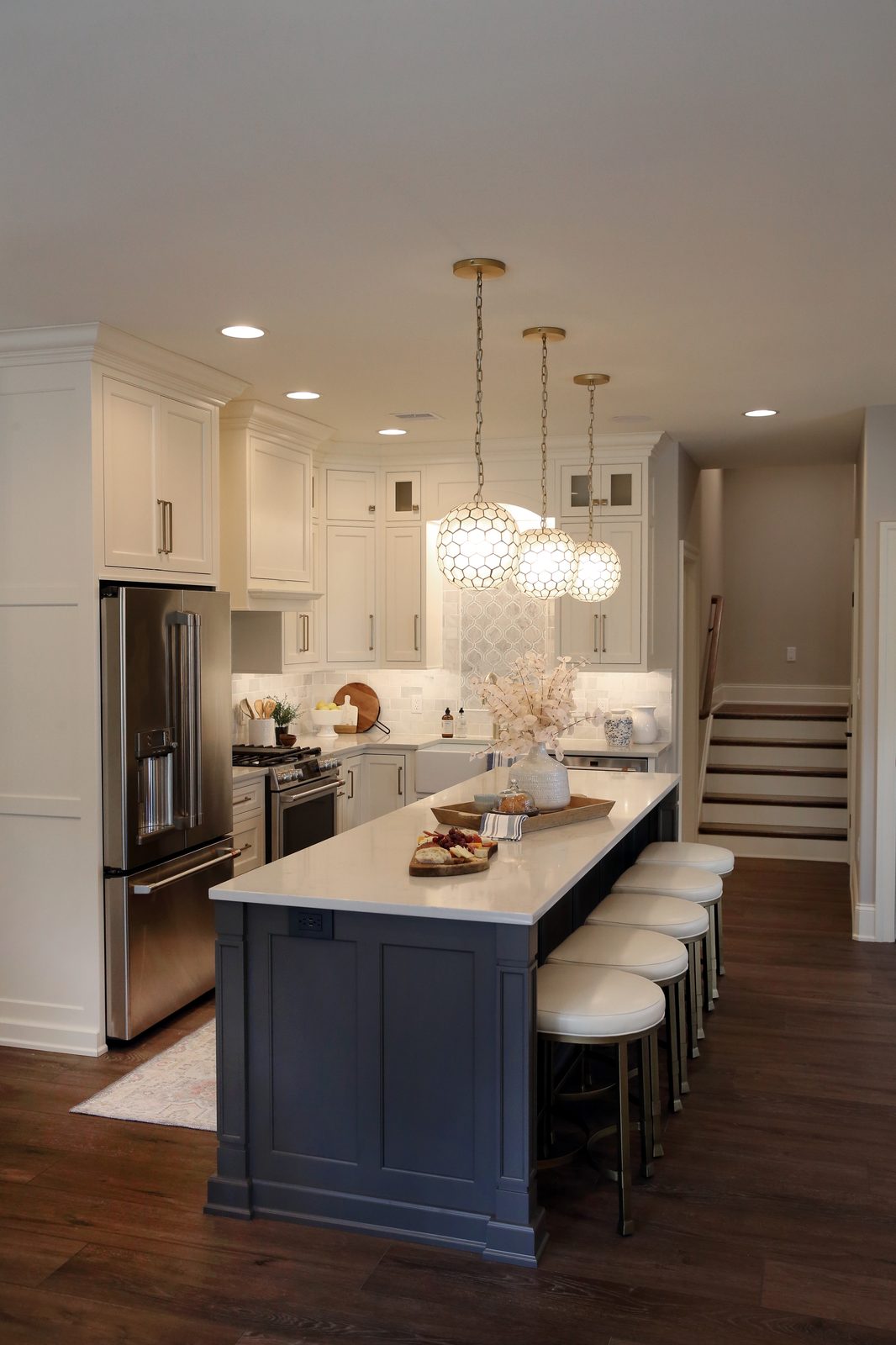 Open kitchen with white cabinetry, navy island, and gold pendant lights